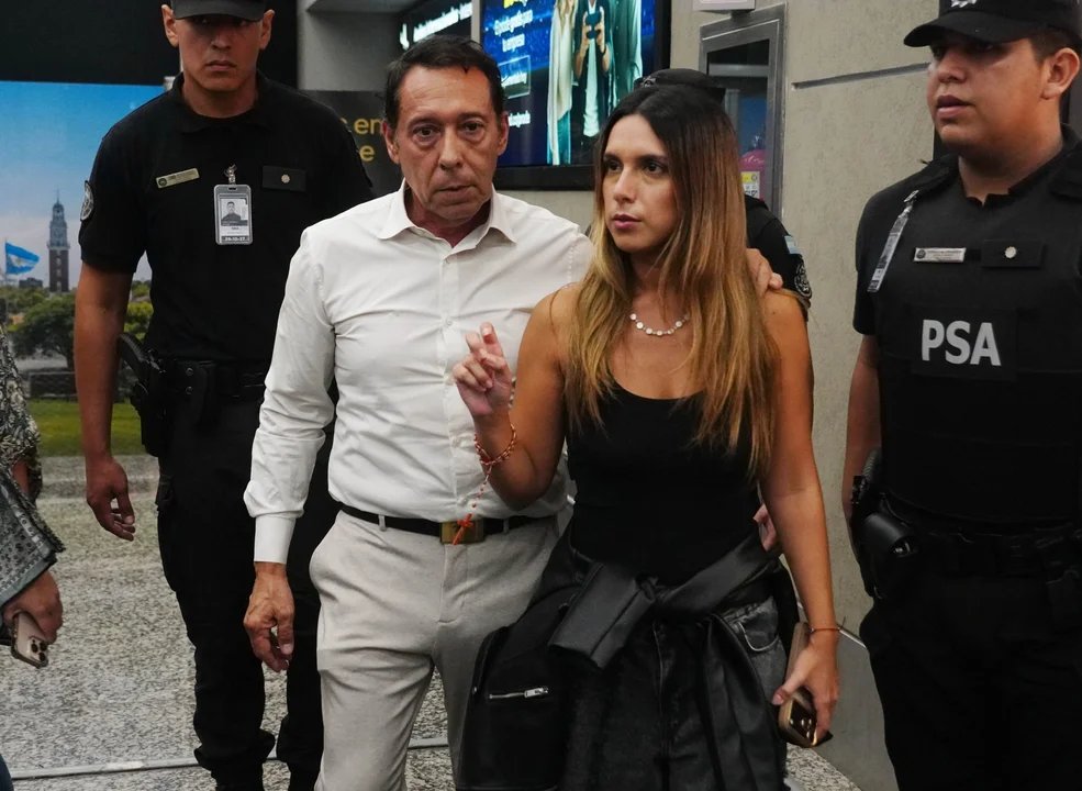 Un hombre y una mujer caminan acompañados por agentes de seguridad en una terminal
