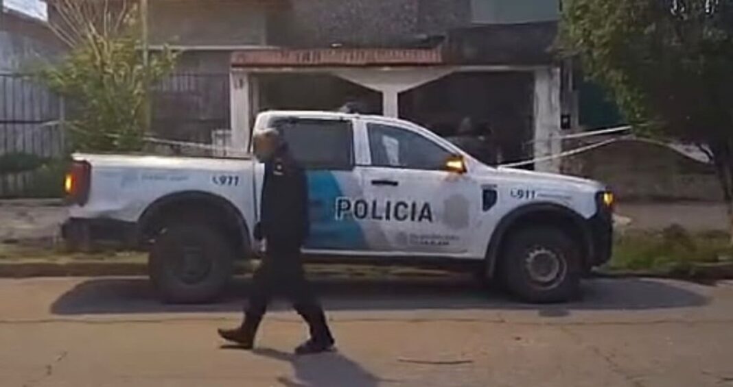 Un policía camina junto a un patrullero estacionado frente a una vivienda con cinta de seguridad